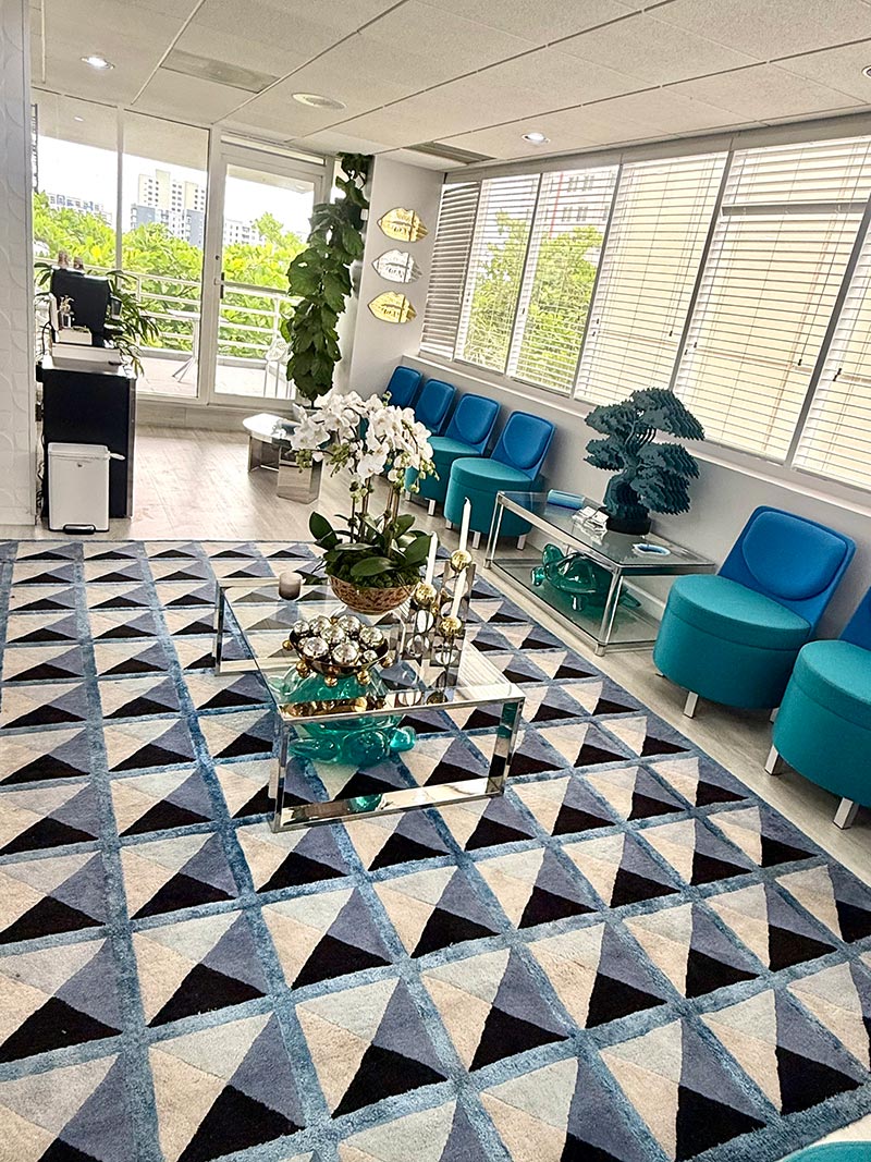 The image shows a modern interior space with geometric patterned flooring, contemporary furniture, and decorative elements such as plants and a vase.